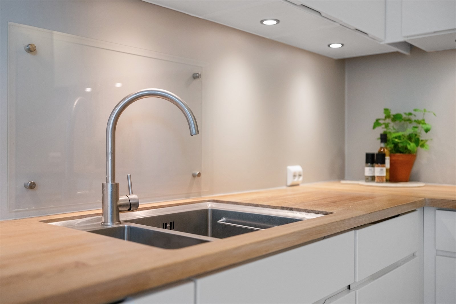 Kjøkkeninnredning med benkeplater av heltre, slette skapfronter, backsplash av glassplater og ventilator med utkast til friluft via viften på loftet(villavent). Galleribilde