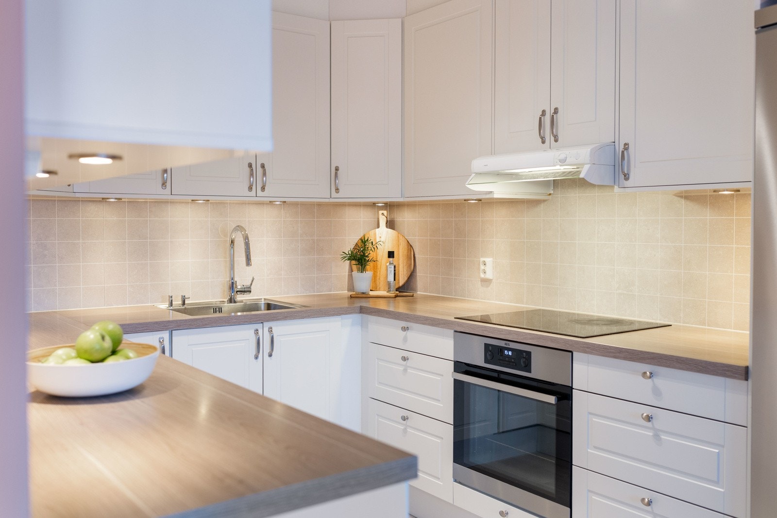 Lyst og moderne kjøkken med integrerte hvitevarer, lyse fliser over benk og godt med skapplass. Galleribilde