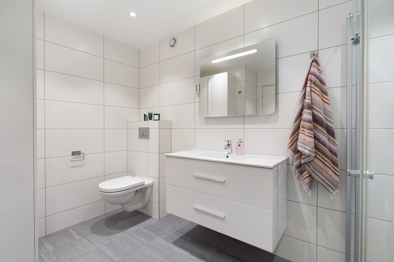 Stor servant med skuffer og speil med belysning. Lyse fliser på veggene og mørke fliser på gulvet Galleribilde