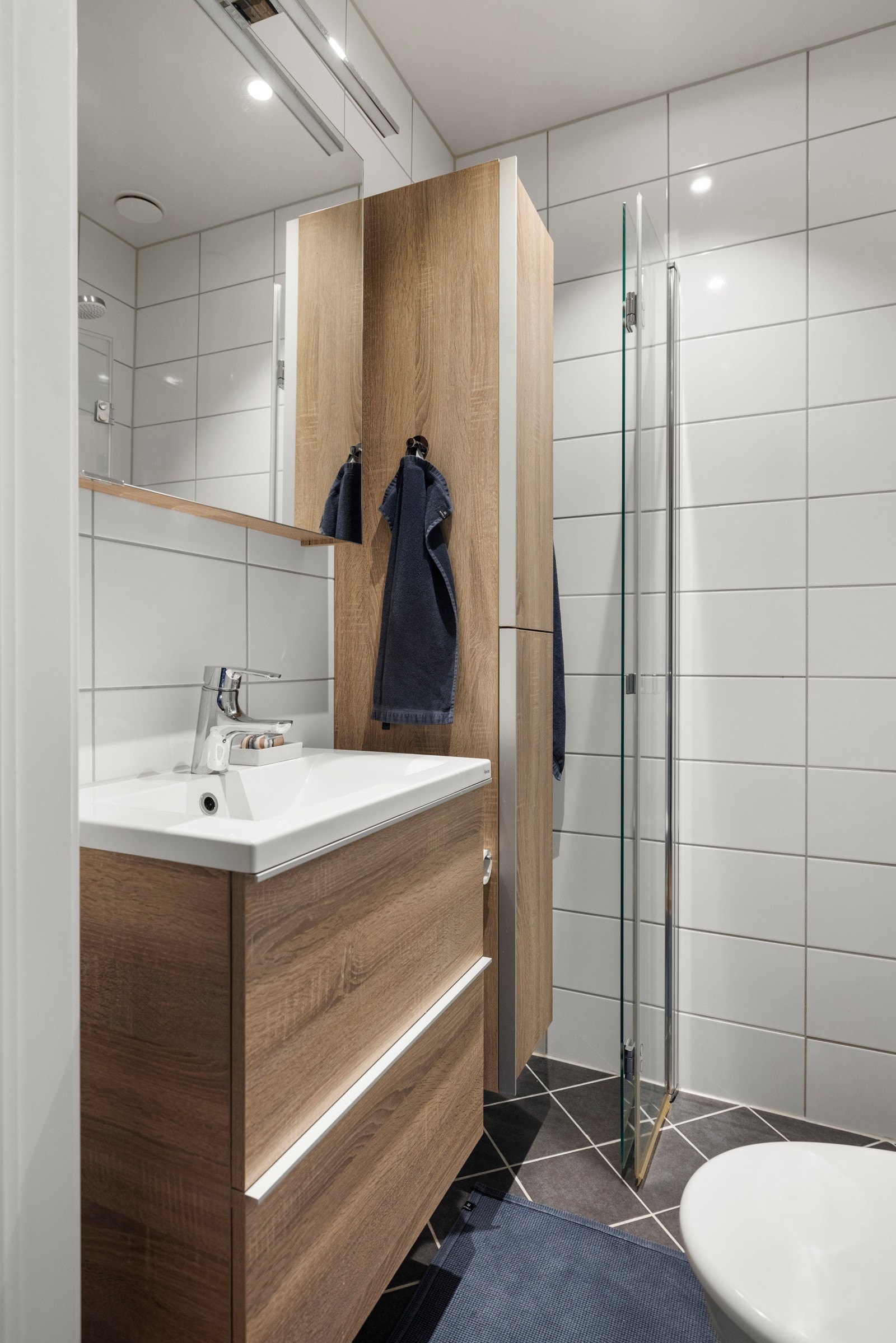 - Baderomsinnredning bestående av benkeskap og høyskap med glatte fronter. Veggskap med speilfronter og belysning over servant. Dusj med innfellbare dører i herdet glass, servant og veggfestet klosett med innebygget sisterne - Galleribilde