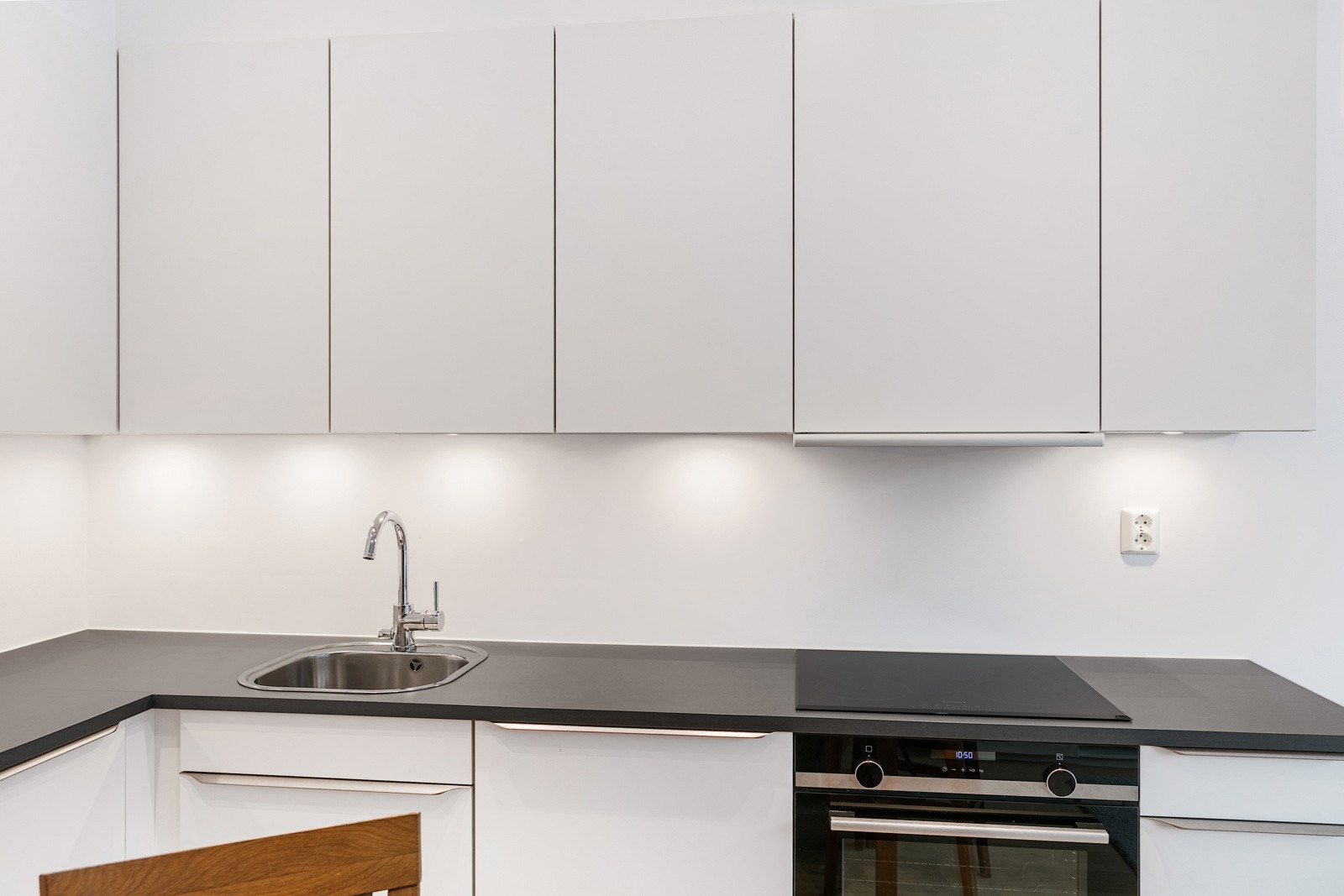 Innredningen har glatte hvite fronter og benkeplater av mørk laminat med vask i stål Galleribilde