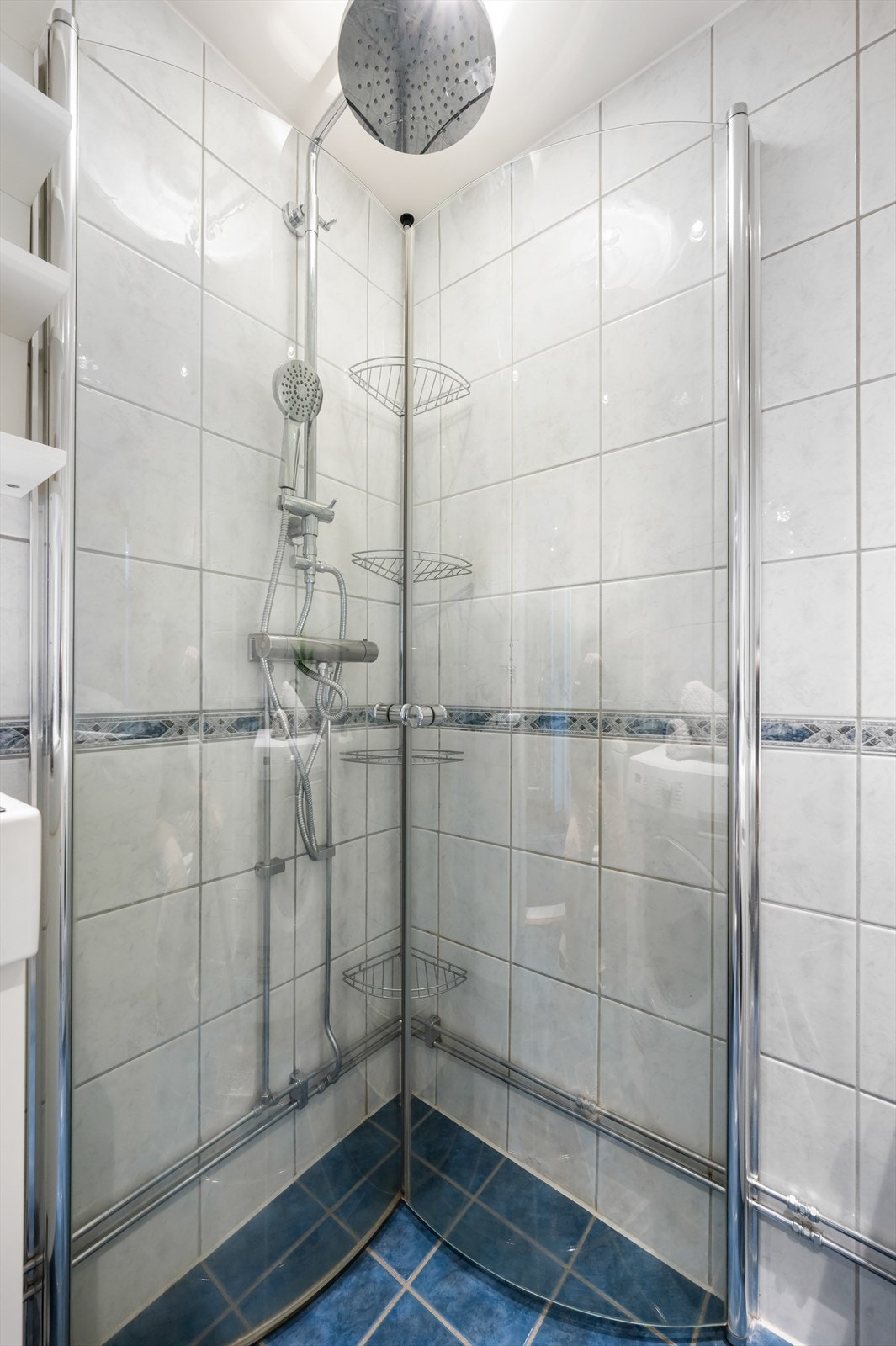 Baderomsinnredning med vegghengt servant på servantskap, gulvstående toalett og dusjhjørne med innfellbare glassdører. Galleribilde