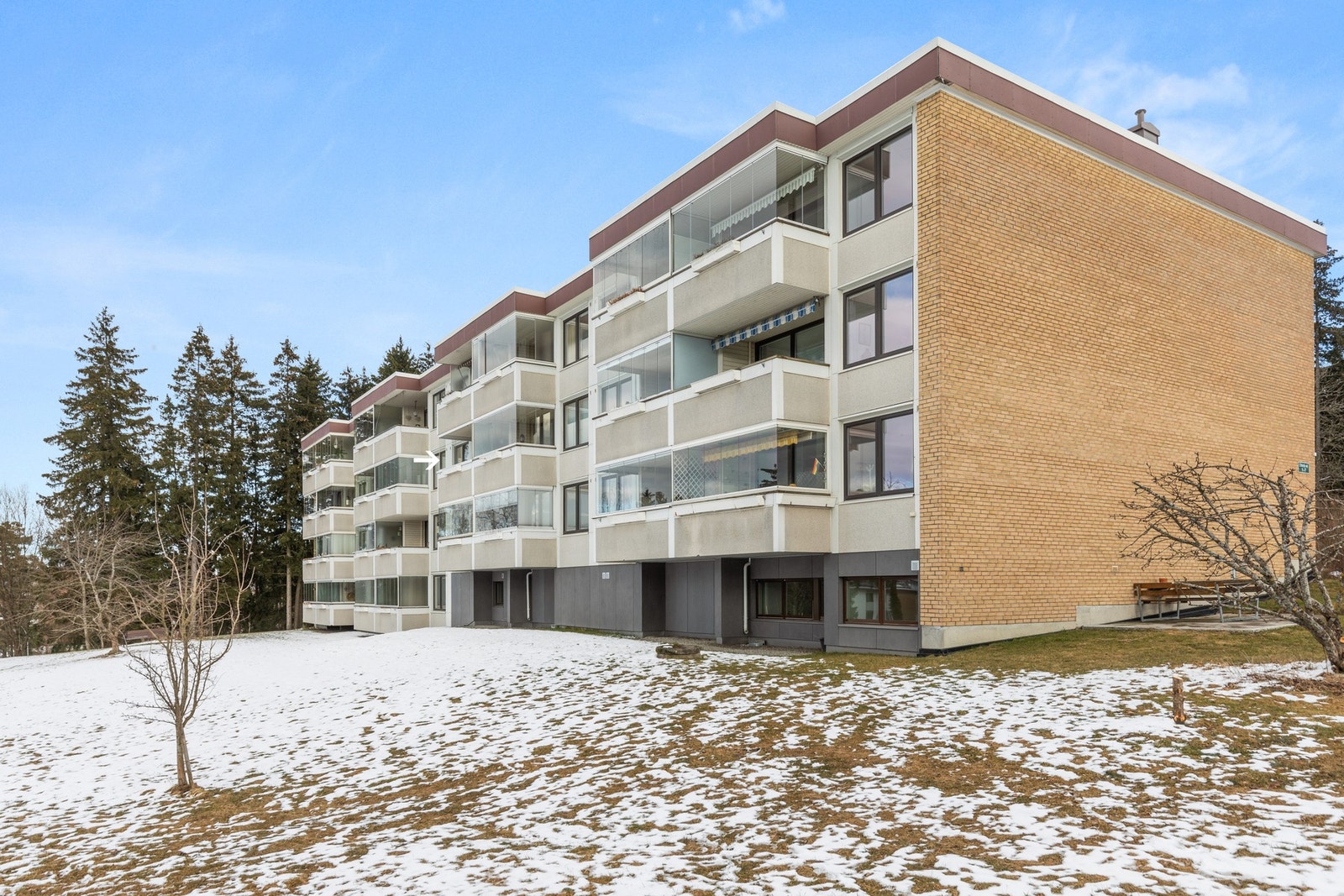 Fasade vist fra balkongsiden, hvor leiligheten fremstår som 3. etasje siden blokken ligger i skrånet terreng. Leiligheten er markert med pil. Galleribilde