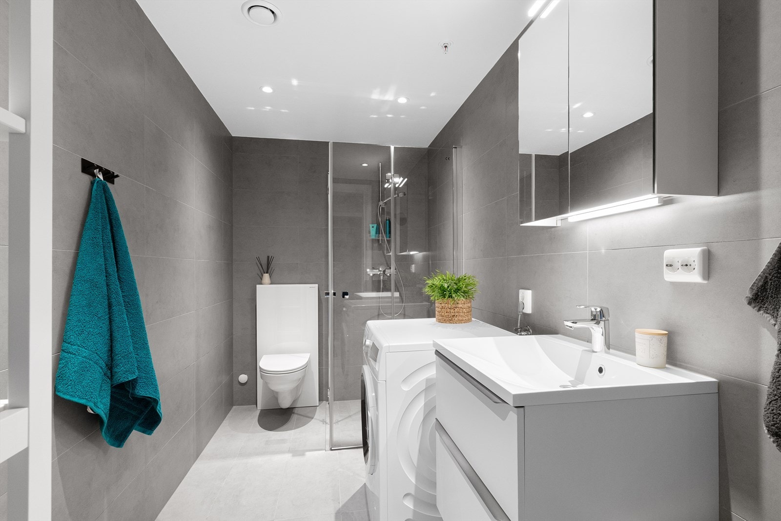 Badet har innredning med nedfelt servant, veggmontert toalett, dusjhjørne og opplegg for vaskemaskin. Galleribilde
