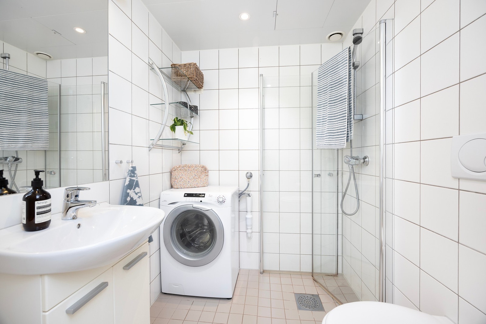 Badet har flislagte flater med dowlights i himling. Badet er innredet med vegghengt servantskap med nedsenket servant, vegghengt speil, dusjhjørne med innfellbare glassdører og vegghengt toalett. Galleribilde