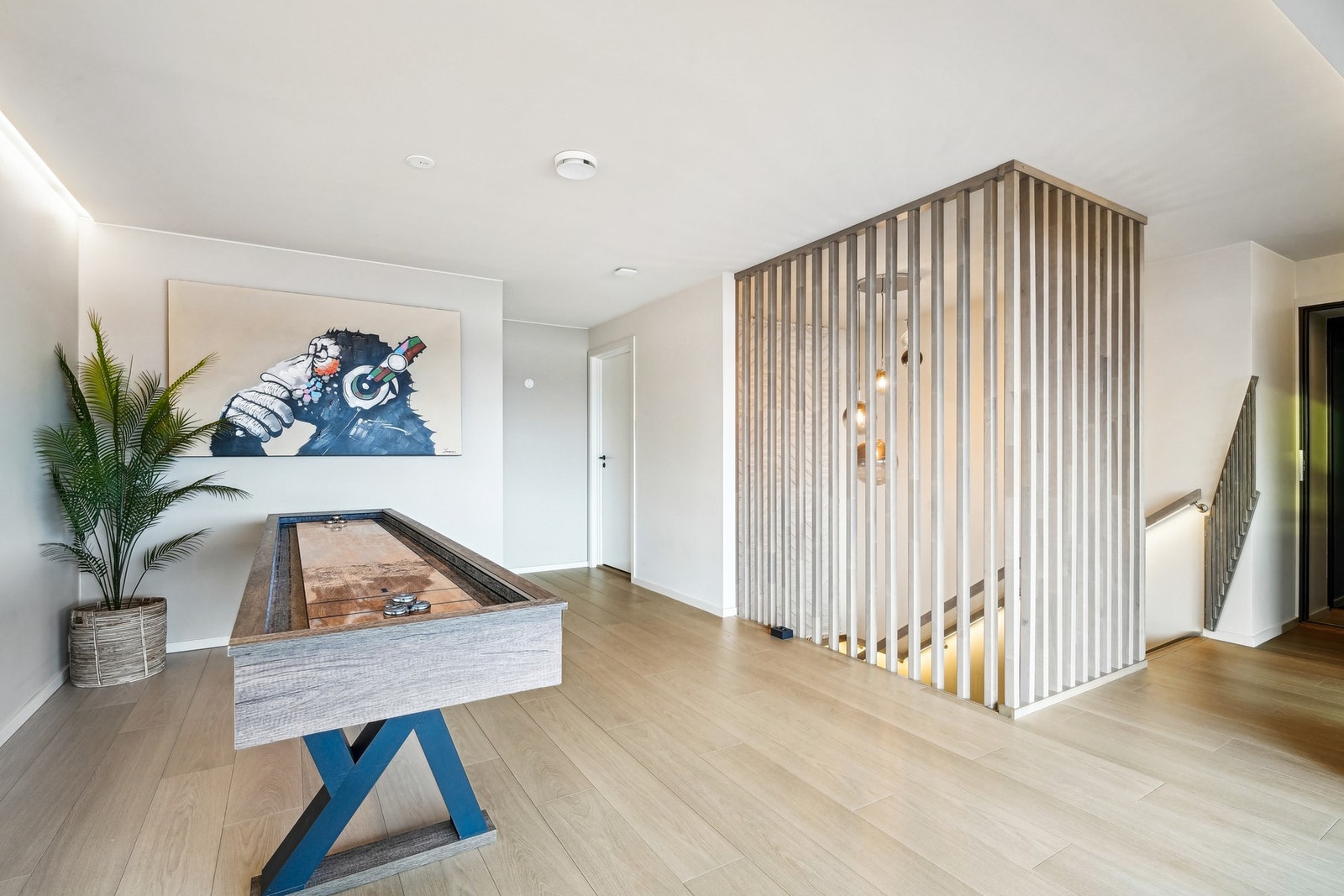 Loftstuen er lys og luftig med spilevegg mot trapperommet, indirekte belysning langs tak og inngang til et hobbyrom. Galleribilde