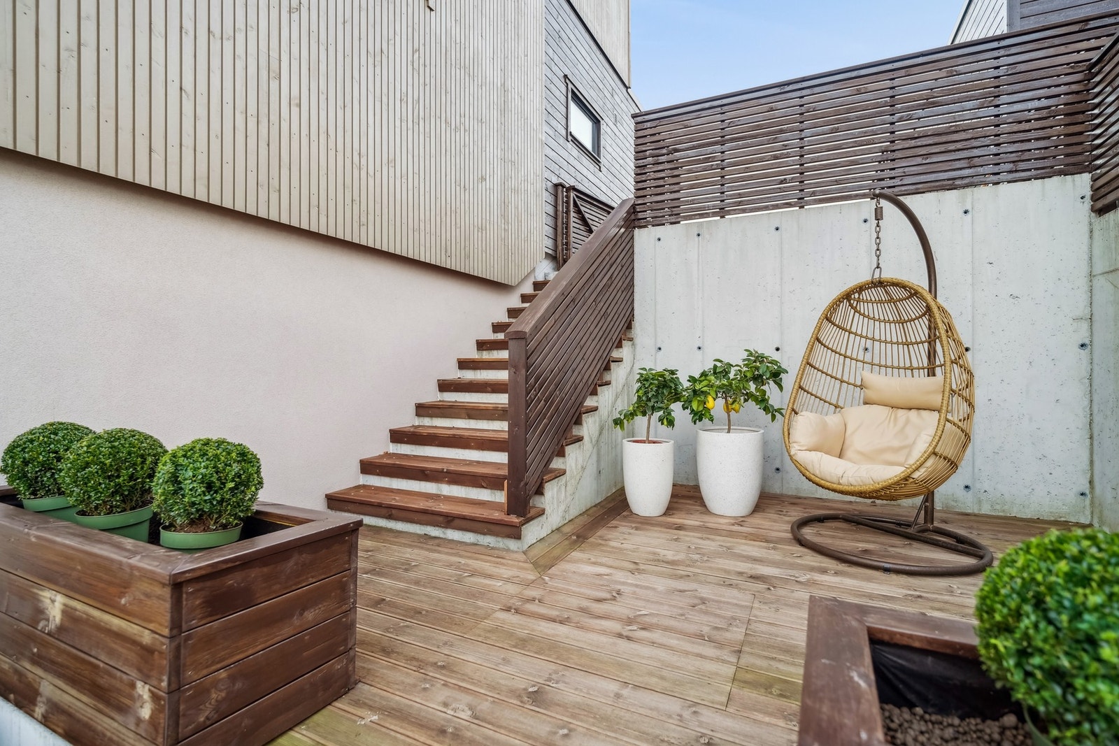 En moderne og stilfull terrasse med naturlige trematerialer, grønne planter og en koselig hengestol - perfekt for avslapning i en rolig utendørs atmosfære. Galleribilde