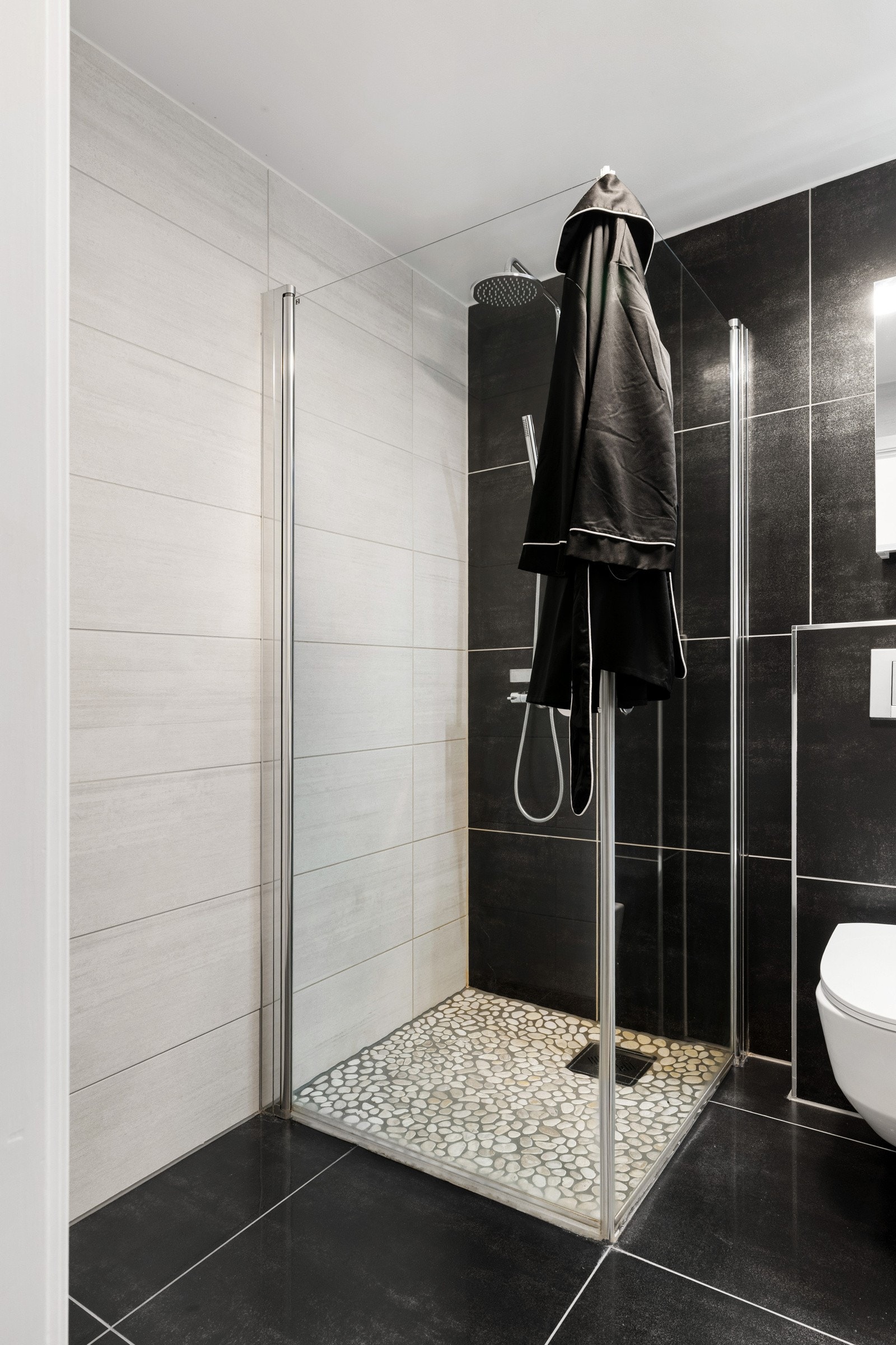 Badet er utstyrt med vegghengt toalett, opplegg for vaskemaskin og flott dusjhjørne med stilig gulvflate og glassdør. Det er selvfølgelig behagelig gulvvarme. Galleribilde