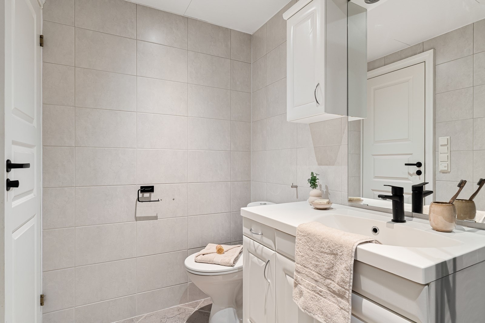 Badet har en tidløs og klassisk innredning med lyse fliser og skap, i tillegg til sorte detaljer. Galleribilde