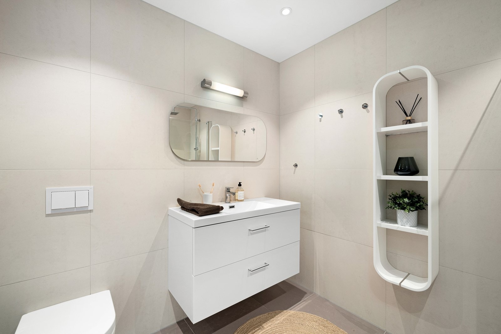 Badet er innredet med vegghengt toalett, dusj med glass foldedører, servant med møblement, speil og belysning. Galleribilde