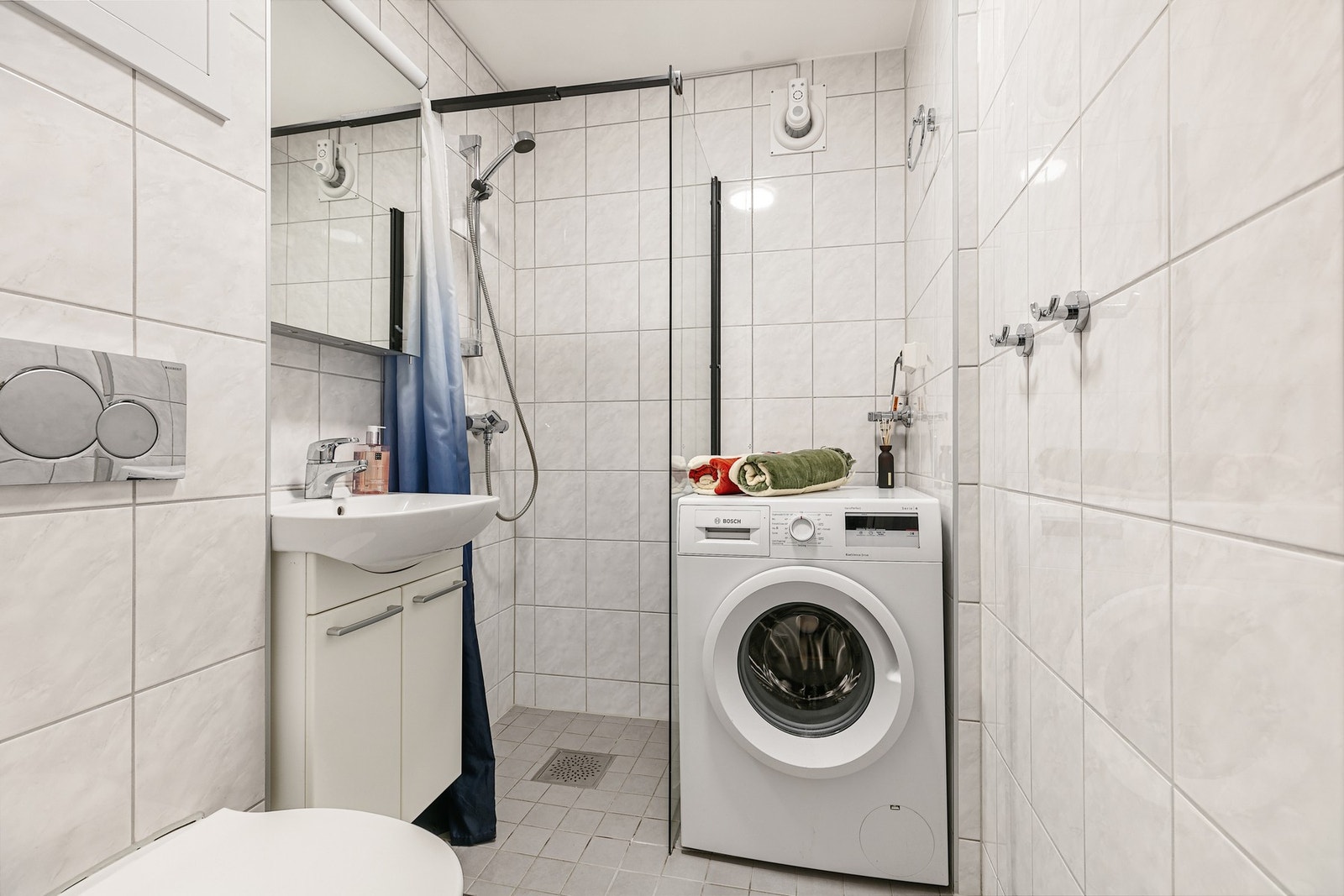 Badet er innredet med vegghengt toalett, servant med underskap/speilskap og et dusjhjørne med glassvegg Galleribilde