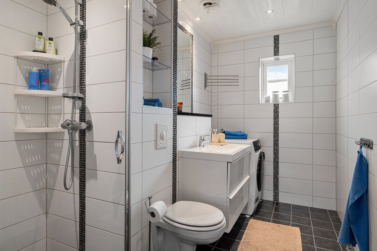 Pent flislagt bad med varme i gulv. Rommet er utstyrt med servant, servantskap, vegghengt toalett, dusjhjørne og plass for vaskemaskin. Galleribilde