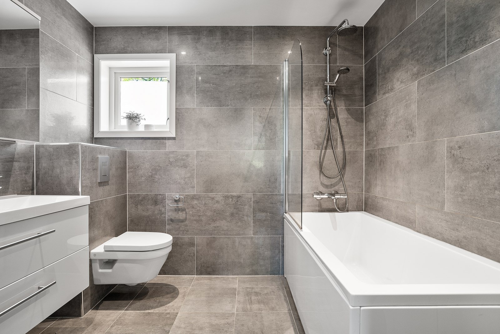 Badet er innredet med servantskap, servant med dobbelservant over, veggmontert wc og badekar. Galleribilde