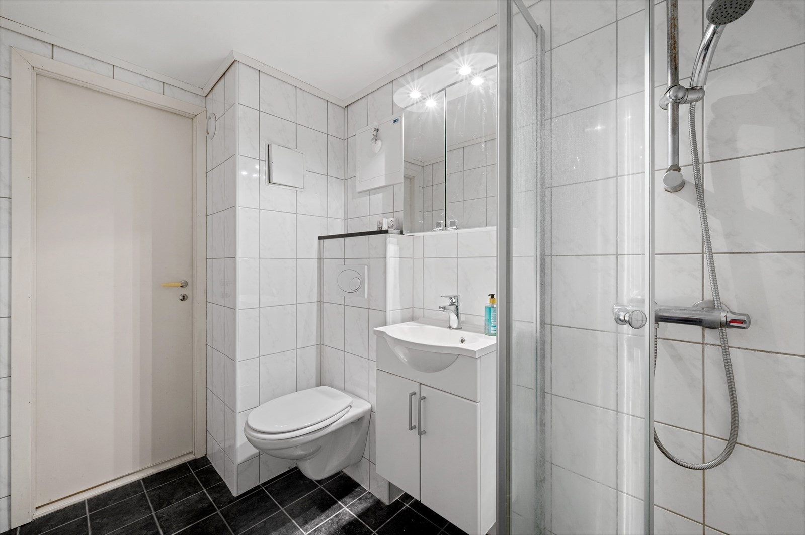 Baderommet er innredet med vegghengt toalett, dusjhjørne m/glassdører og servant med innredning, speil og belysning. Galleribilde