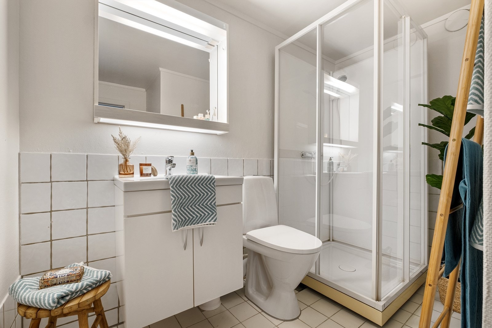 Baderom med flislagt gulv og deler av vegg og varmekabler i gulv. Badet er innredet med servant med underskuffer, speil, dusjhjørne og toalett. Galleribilde