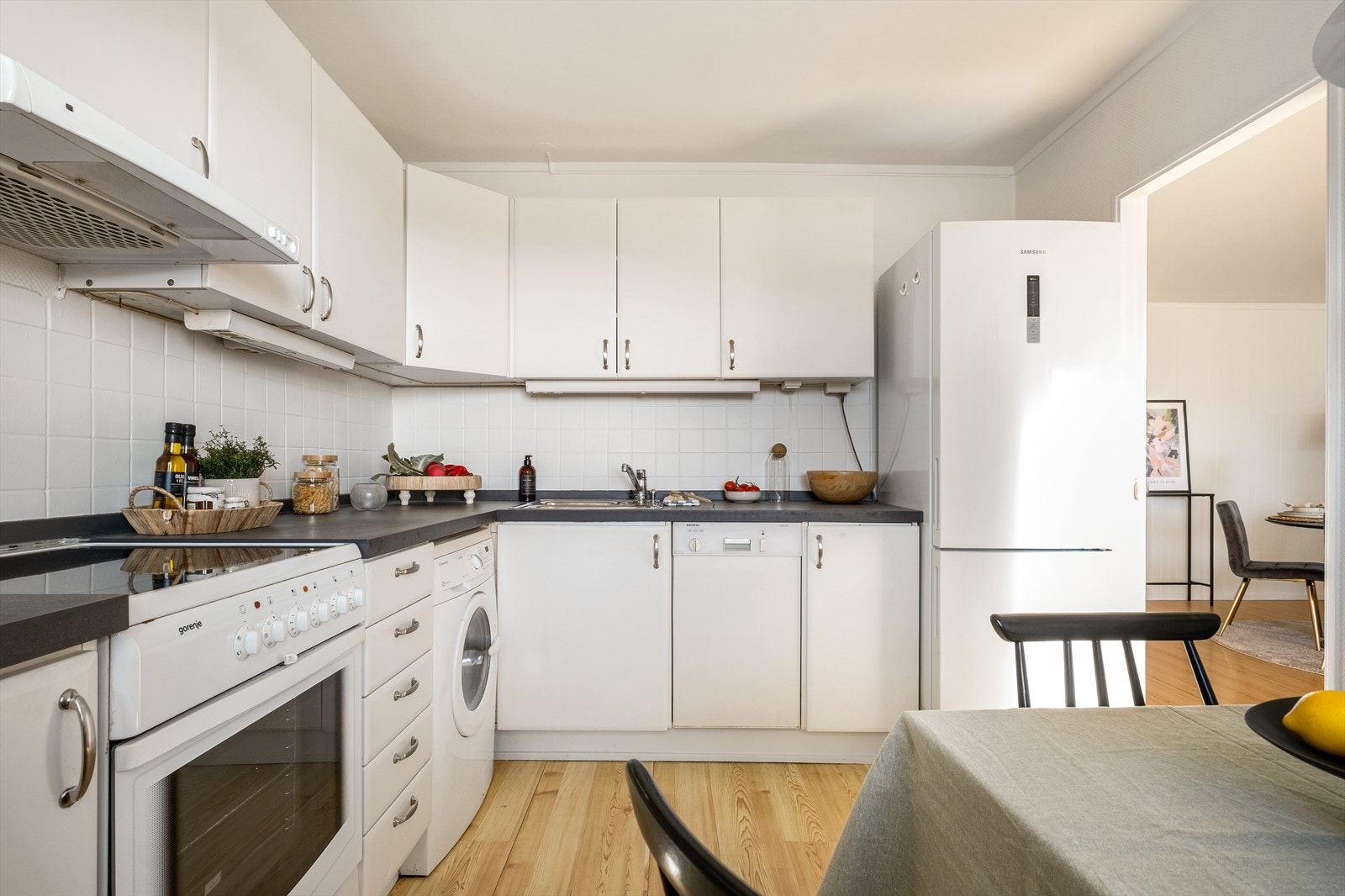 Kjøkkeninnredning med malte slett flater og laminat benkeplate. Frittstående hvitevarer som kjøl/frys, komfyr og oppvaskmaskin. Opplegg for vaskemaskin. Galleribilde