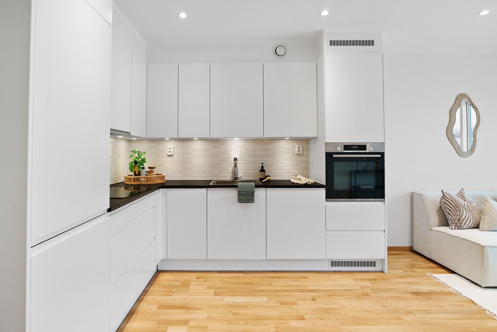 Pent og tidløst kjøkken med hvite slette fronter og benkeplate av laminat. Fliser på vegg over benk. Downlights under overskap. Galleribilde