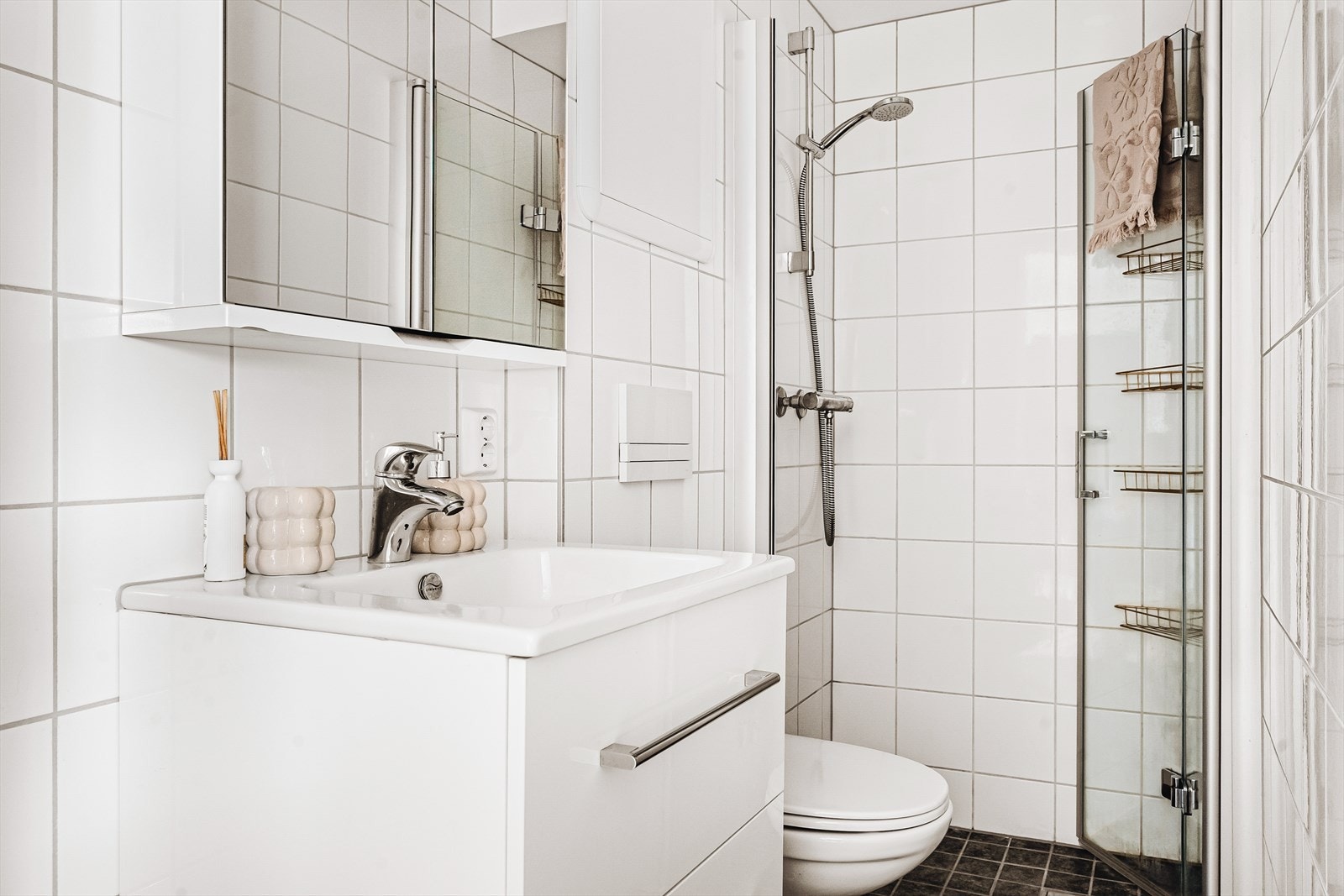 Badet er helfliset og har varme i gulvet. Nedsenket dusjsone i enden av baderom. Det er videre servant med skapsseksjon samt vegghengt toalett. Galleribilde