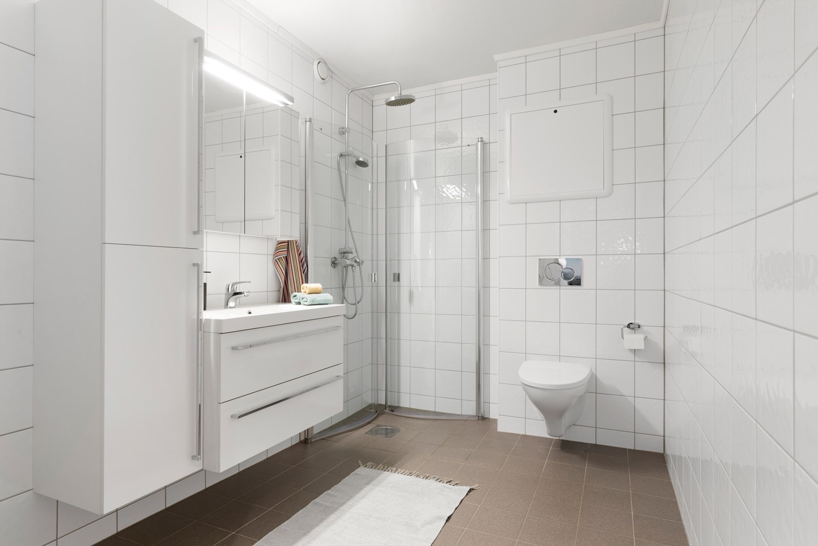 Badet har malt tak, flislagte vegger og gulv, samt baderomsinnredning med vegghengt WC og dusjvegger. Galleribilde