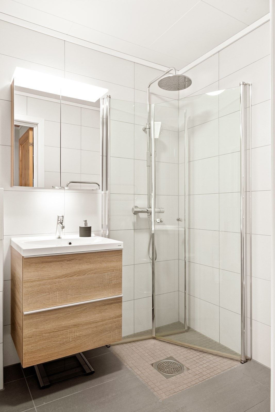 Badet er moderne og stilrent, innredet med servant i seksjon med speil, vegghengt WC og dusjhjørne med innfellbare glassdører. Galleribilde