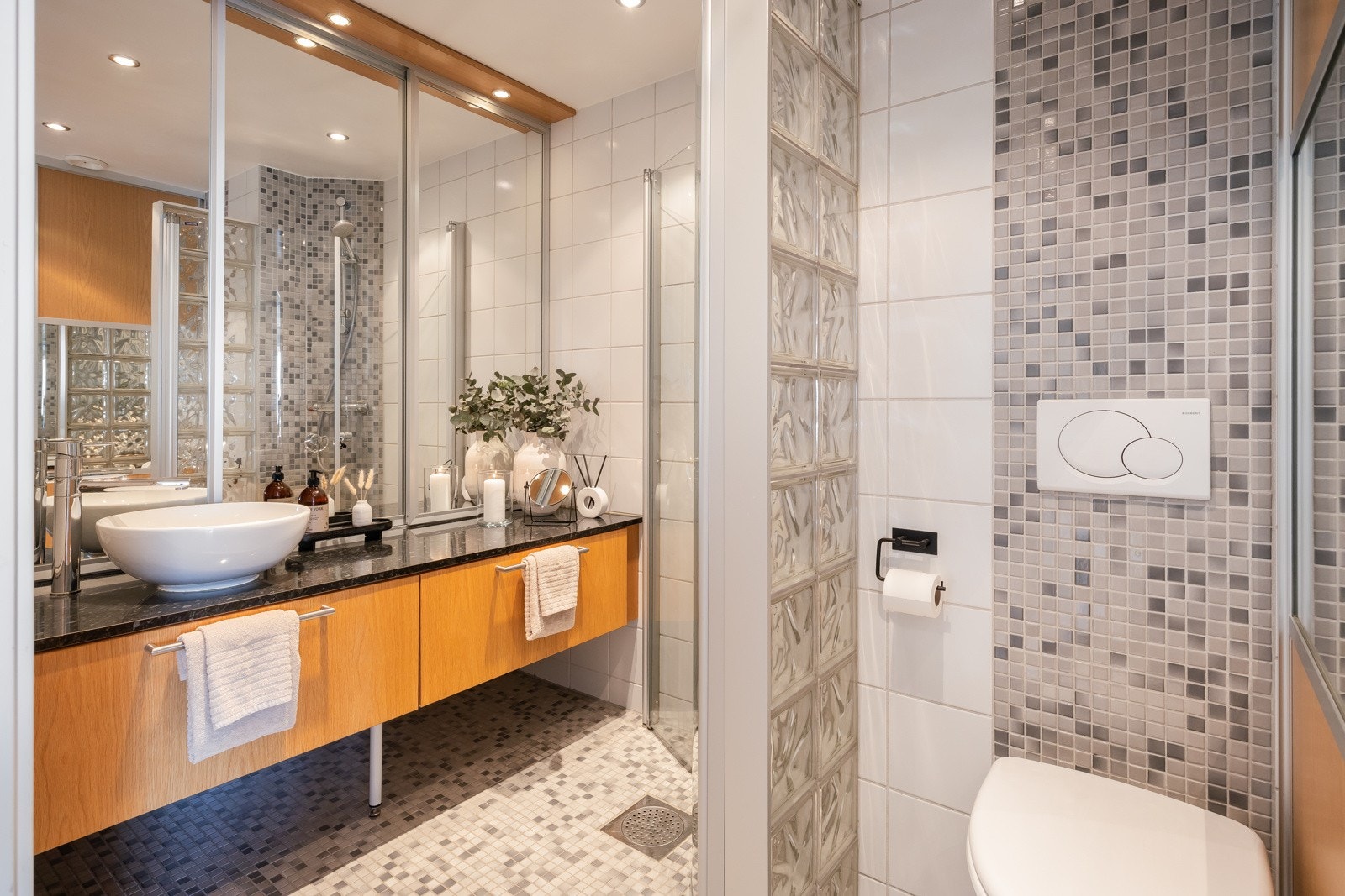 Flislagt baderom som er praktisk inndelt i to soner med servant og dusjhjørne i den ene delen, og toalett samt vaskeseksjon i den andre. Galleribilde