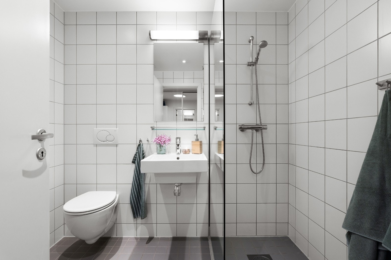 Flislagt baderom utført i lyse farger fra byggeår med vannbåren varme i gulv. Oppbevaring i høyskap og skap på vegg Galleribilde