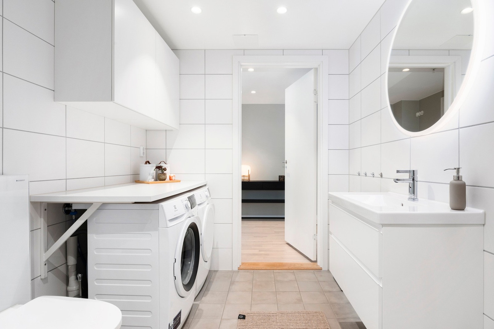 Badet er lyst og moderne, et kombinert vaskerom med nisje for både vaskemaskin og tørketrommel. Galleribilde