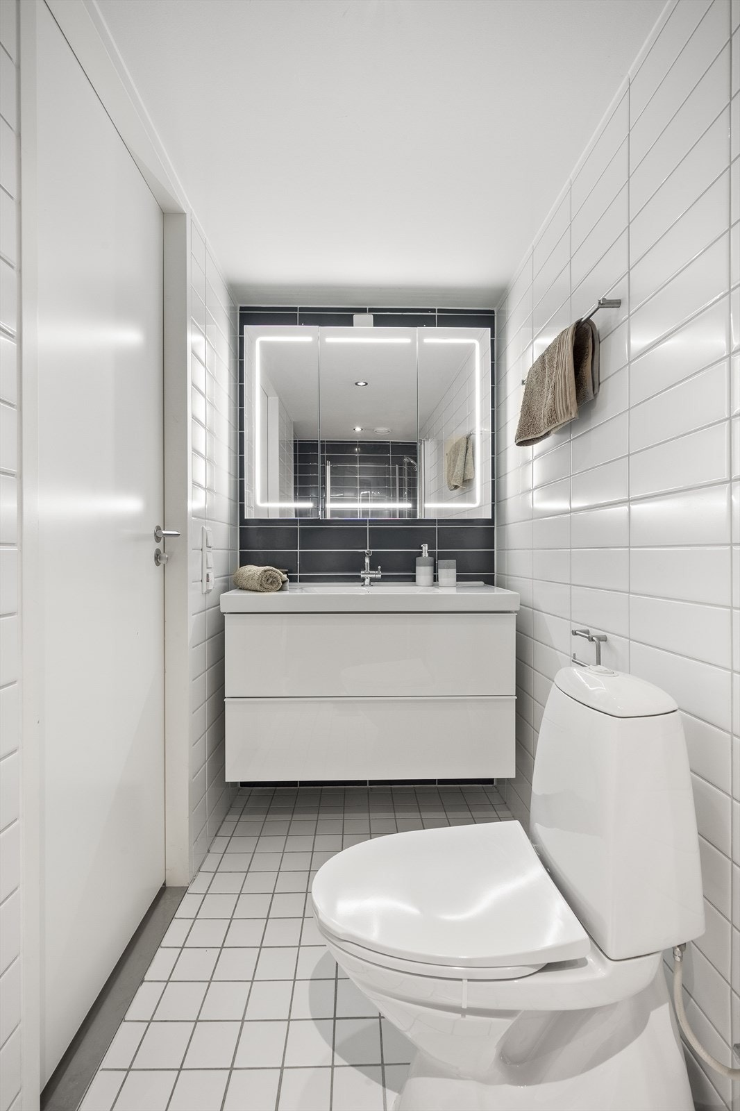 Badet er innredet med klosett, servant med innredning, speil med lys og dusjhjørne med svingbare glassdører. Galleribilde