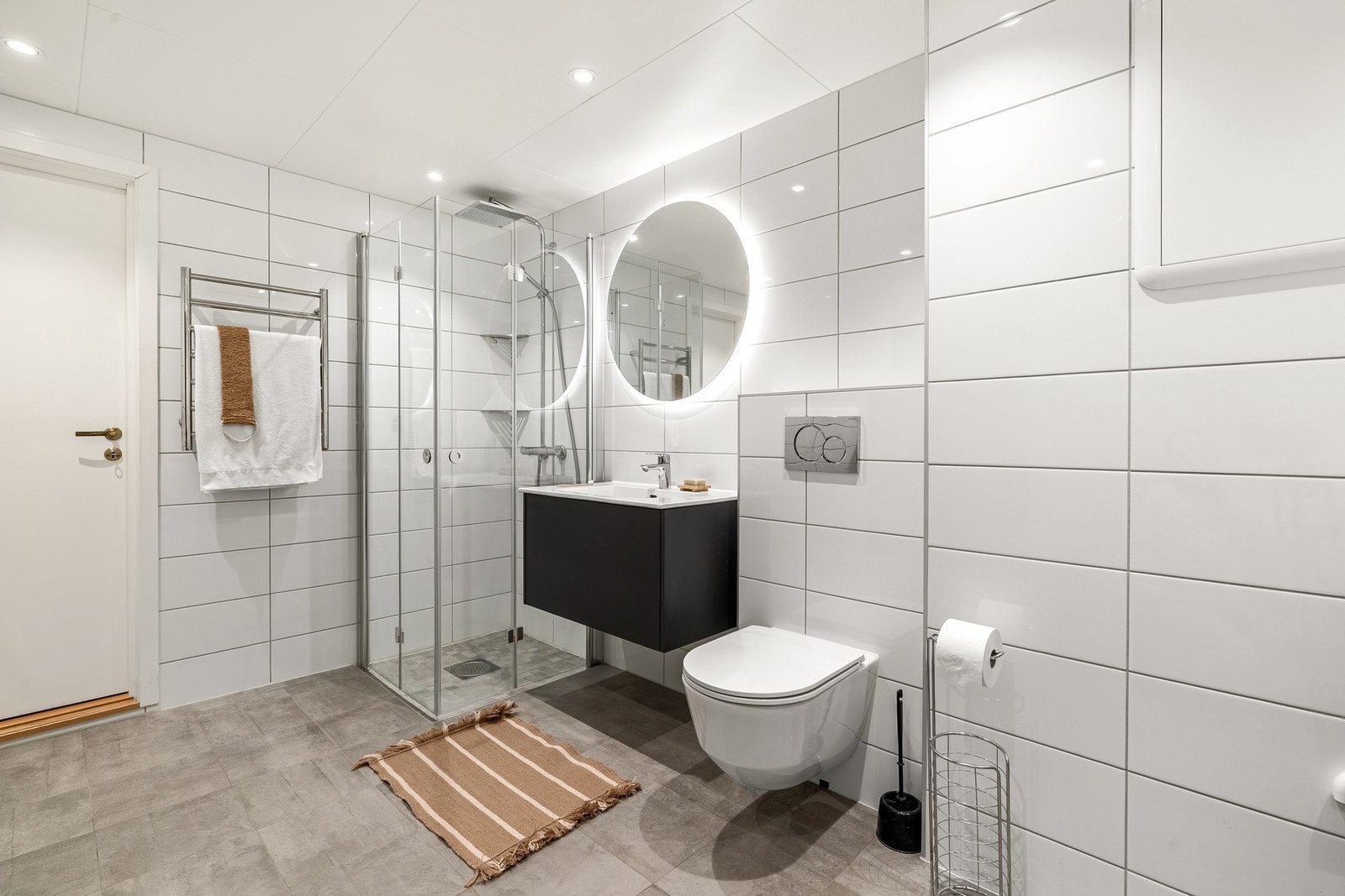 Badet er innredet med vegghengt toalett, servantmøbel med skuffer og speil med integrert belysning, dusj med innfellbare glassvegger. Galleribilde