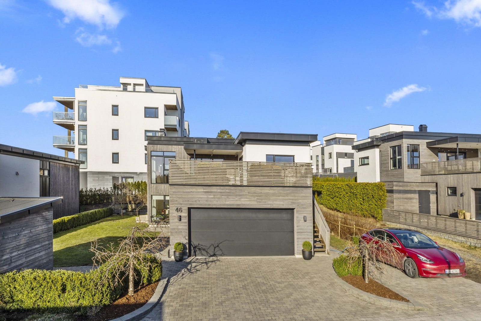 Gårdstun belagt med belegningssteiner og med en estetisk utforming av beplantningen som hekk og trær. Galleribilde