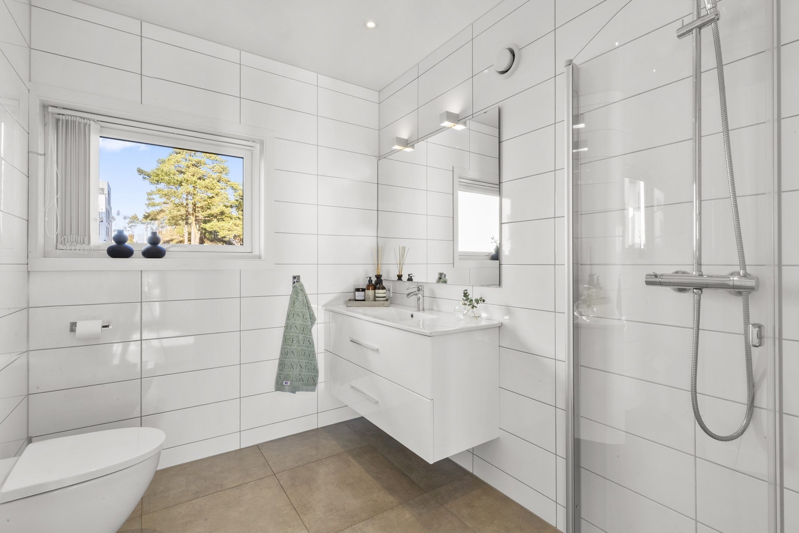 Flislagt baderom i tilknytning til hovedsoverommet. Innfellbare dusjvegger, vegghengt toalett og servant med innredning. Rommet varmes opp med varmekabler. Galleribilde