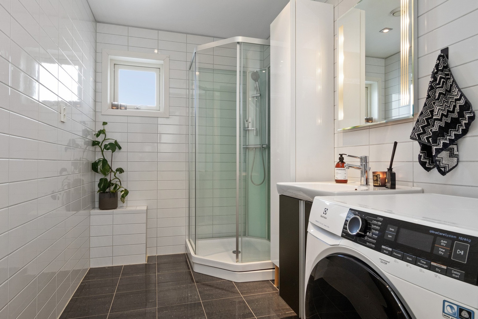 Bad/vaskerom i hendig tilknytning til entreen, og har hvite fliser på veggene, downlights i himlingen og grå fliser på gulv med gulvvarme. Galleribilde