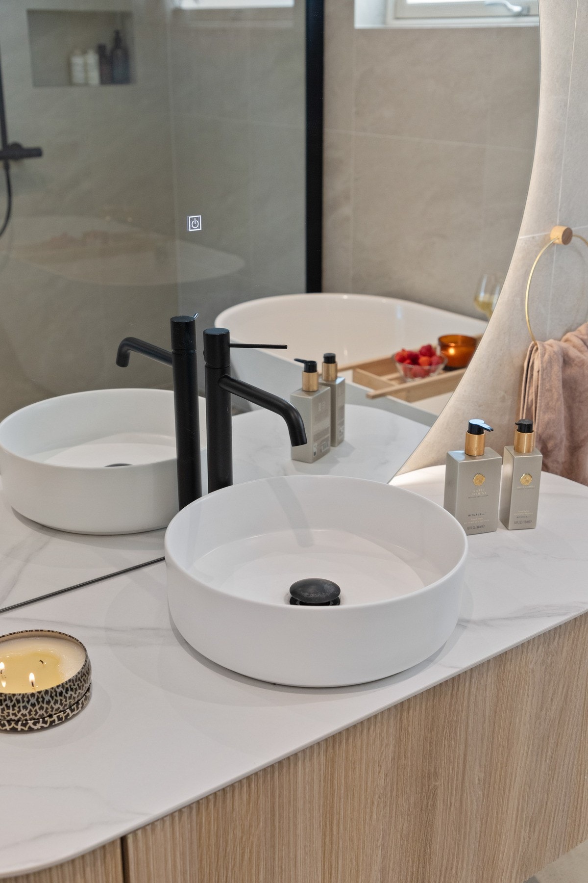 Den moderne baderomsinnredningen har lyse, finerte fronter og består av et veggskap, en seksjon med toppmontert servant og et stort, rundt speil med integrert belysning. Galleribilde