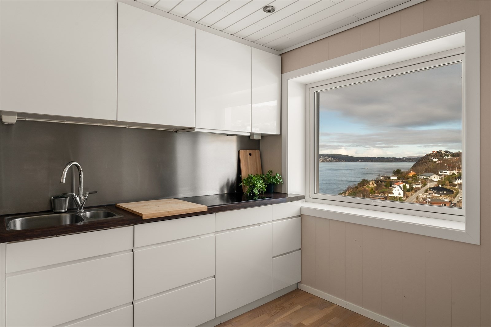 Pen kjøkkeninnredning fra Kvik med slette fronter i lys høyglans utførelse med takhøye skap. Galleribilde