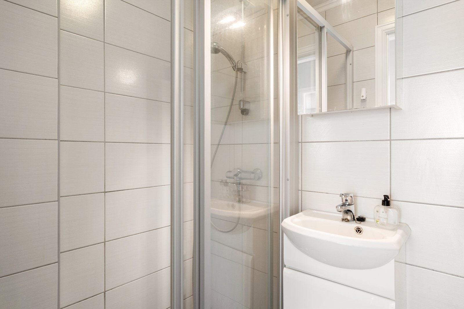 Badet er innredet med dusjvegg av glass, plastsluk med oppsamlerkopp, vegghengt klosett med innebygd sisterne, møblement med servant, overskap med speilfelt og dobbel jordet stikkontakt. Galleribilde