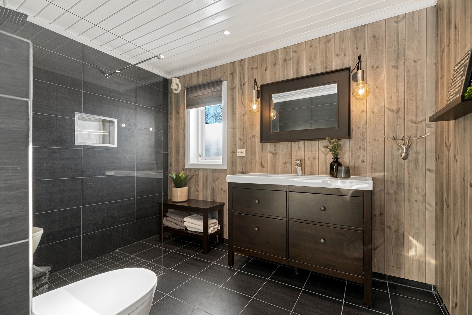 Badet er innredet med vegghengt toalett, dusjkabinett i hjørne og flott servant med speil Galleribilde