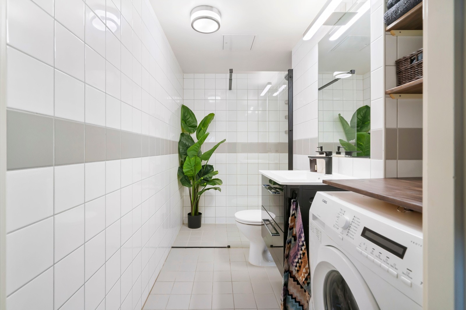 Romslig flislagt baderom. Nyere servantskap med moderne sort blandebatteri og opplegg for vaskemaskin og tørketrommel. Galleribilde