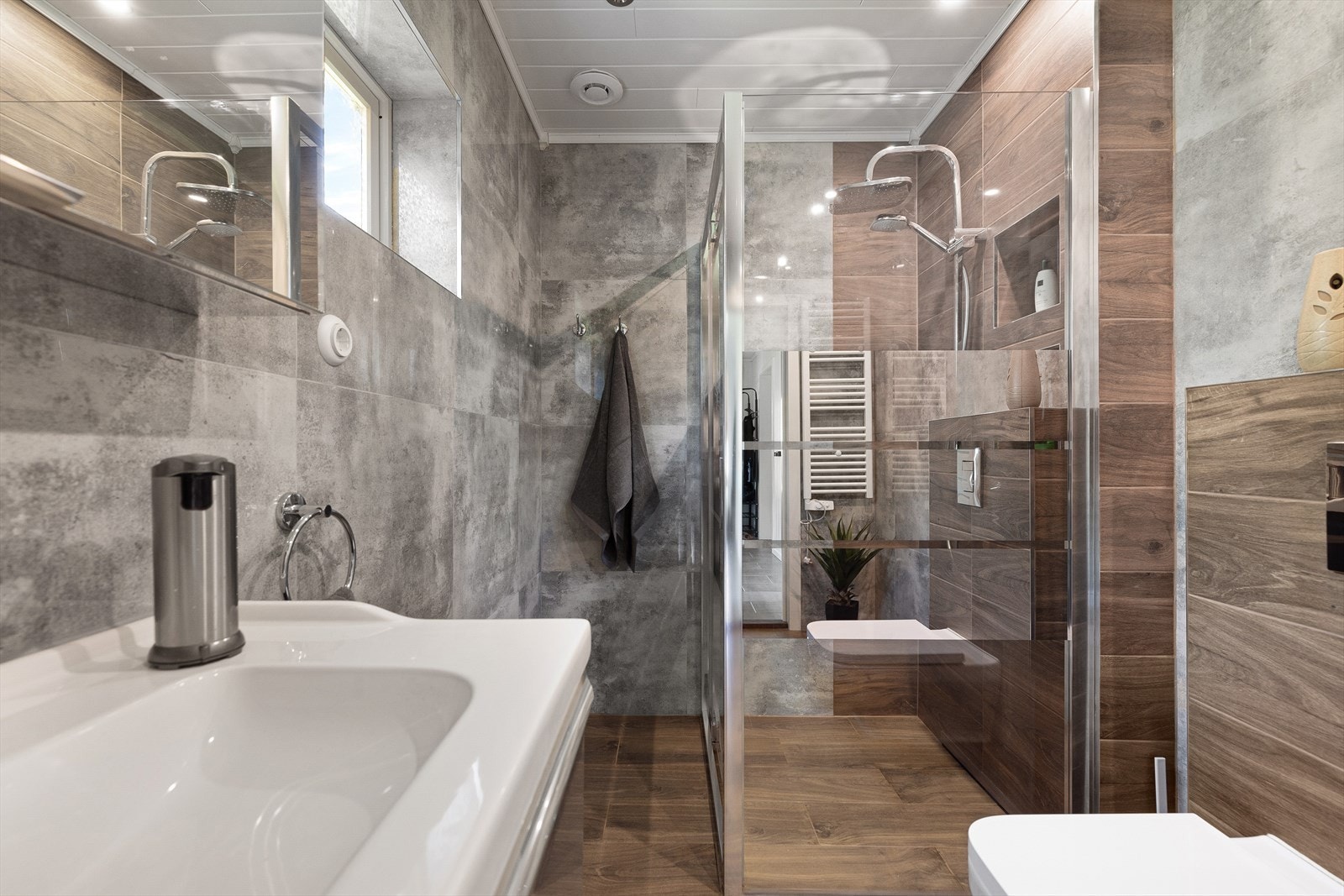 Badet ble pusset opp i 2020/2021. Blank og glanset innredning, veggene dekket av rustikke betongfliser og gulv med tremønstrede fliser. Galleribilde