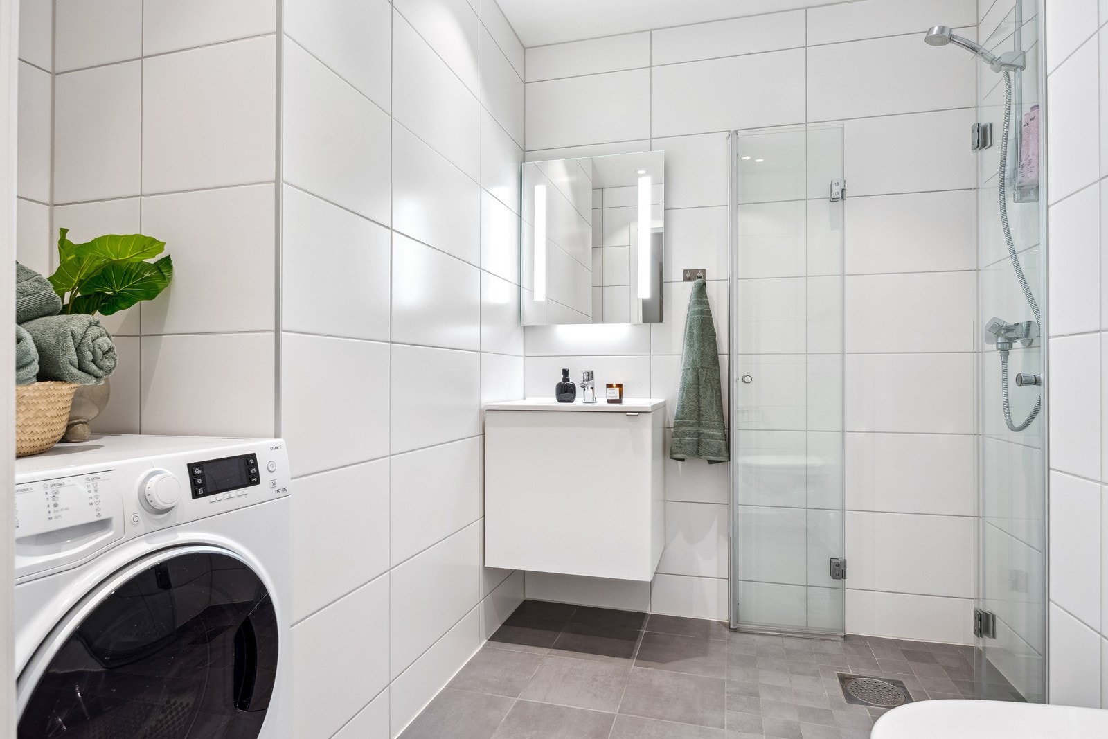 Lekkert baderom med store fliser og dusjhjørne med glassdører, samt opplegg for vaskemaskin. Galleribilde