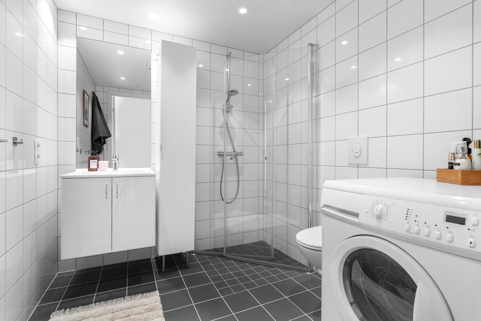 Romslig, flislagt bad med dusjhjørne og opplegg til vaskemaskin Galleribilde