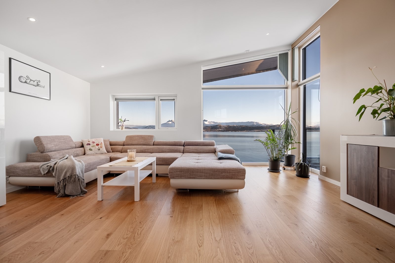 Stuen bades i dagslys fra store panoramavinduer som visuelt gjør havutsikten til en del av rommet. Galleribilde