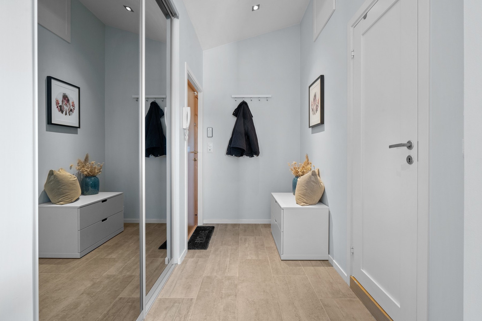 Pen entré med lysmalte vegger, downlights i himlingen og fliser med gulvvarme. Yttertøyet ryddes enkelt bort i en plassbygd skyvedørsgarderobe, Galleribilde