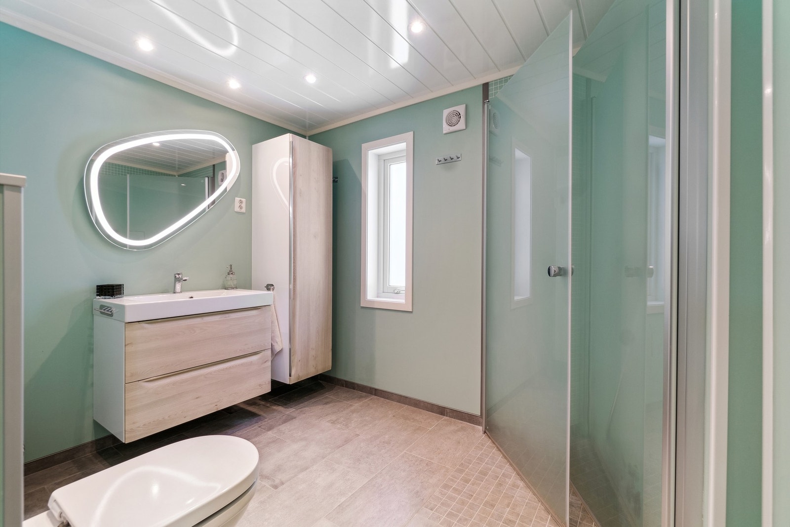 Badet har tidsriktige materialer og farger som skaper en lun atmosfære. Du kan enkelt organisere håndklær, toalettsaker og andre nødvendigheter uten at det går på bekostning av romfølelsen. Galleribilde