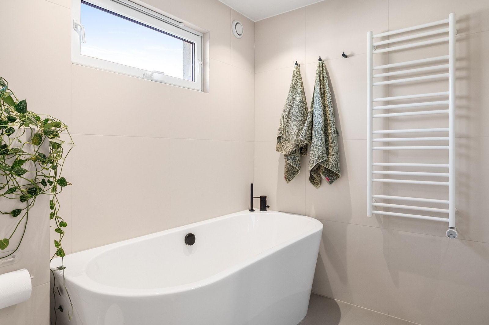 Vinduer på badet sørger for rikelig med dagslys og luftemuligheter. Det er montert vegghengt håndklevarmer mellom badekar og dusj. Galleribilde