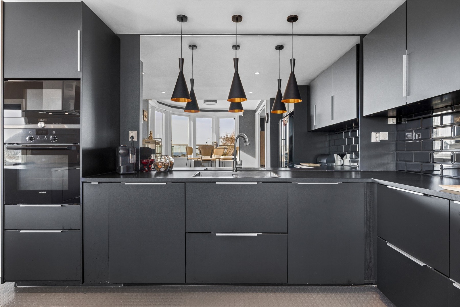 Innredningen er fra 2017, med sorte, glatte fronter og en stor oppvaskkum nedfelt i en benkeplate av laminat. For ekstra romfølelse og et luftigere uttrykk er overskap droppet til fordel for et stort speil på den ene veggen. Galleribilde