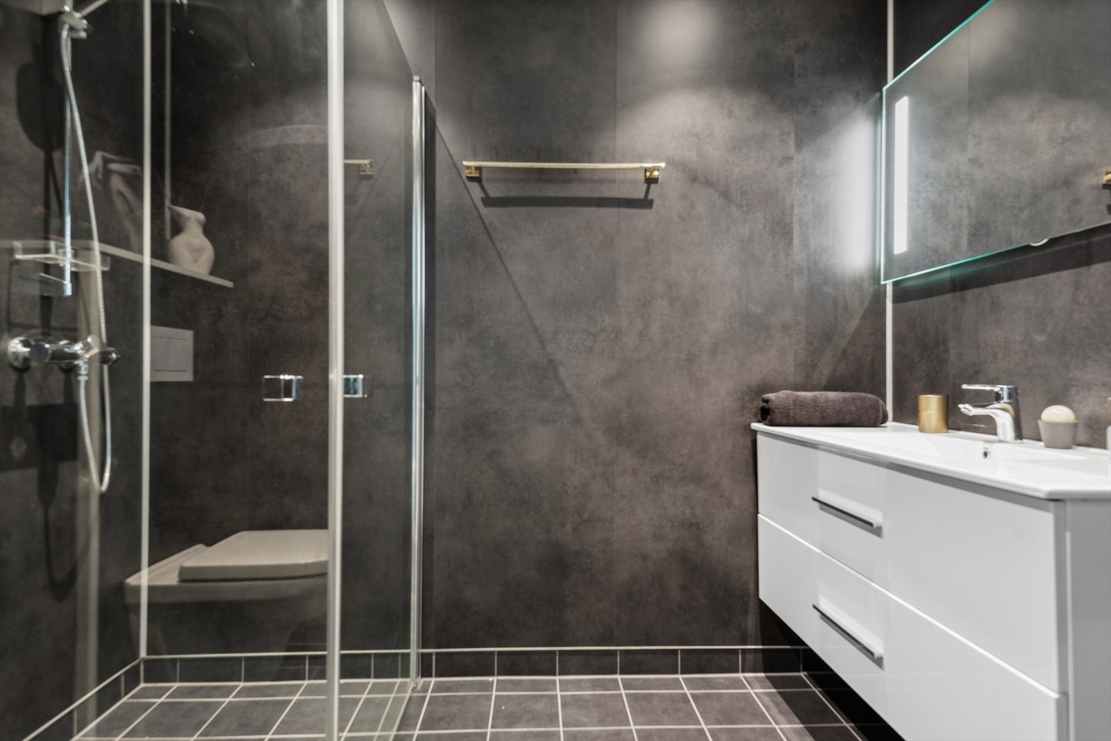 Badet i første etasje har flislagt gulv med varme, mørke, elegante overflater og lys innredning. Galleribilde