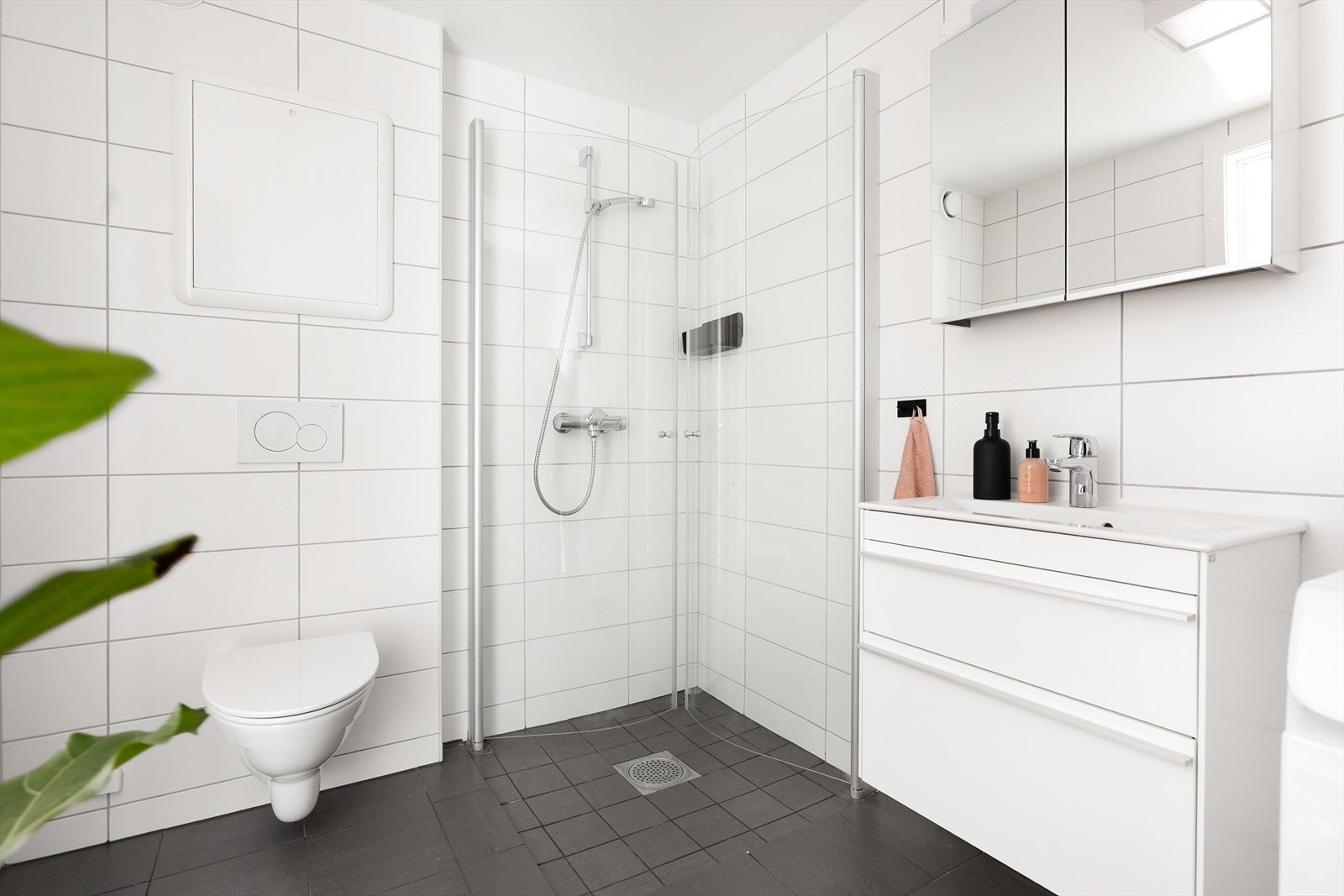 Badet er innredet med vegghengt toalett og en moderne baderomsinnredning med speilskap. Dusjhjørne med innfellbare glassdører Galleribilde