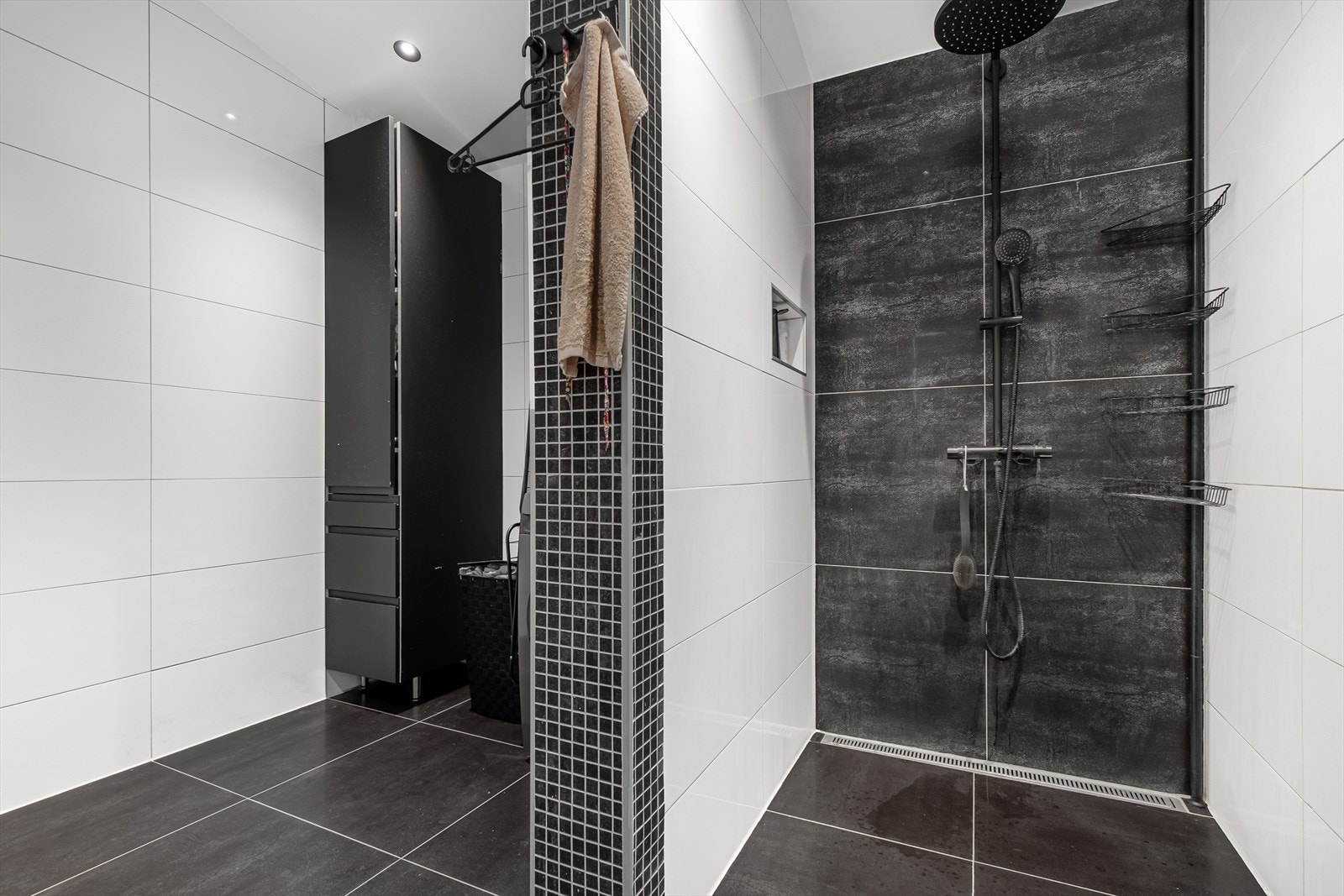 Bad innredet med veggheng wc, innredning med skuffer, speil med skap og lys, langskap, dusjsone med regndusj og opplegg for vaskemaskin. Galleribilde