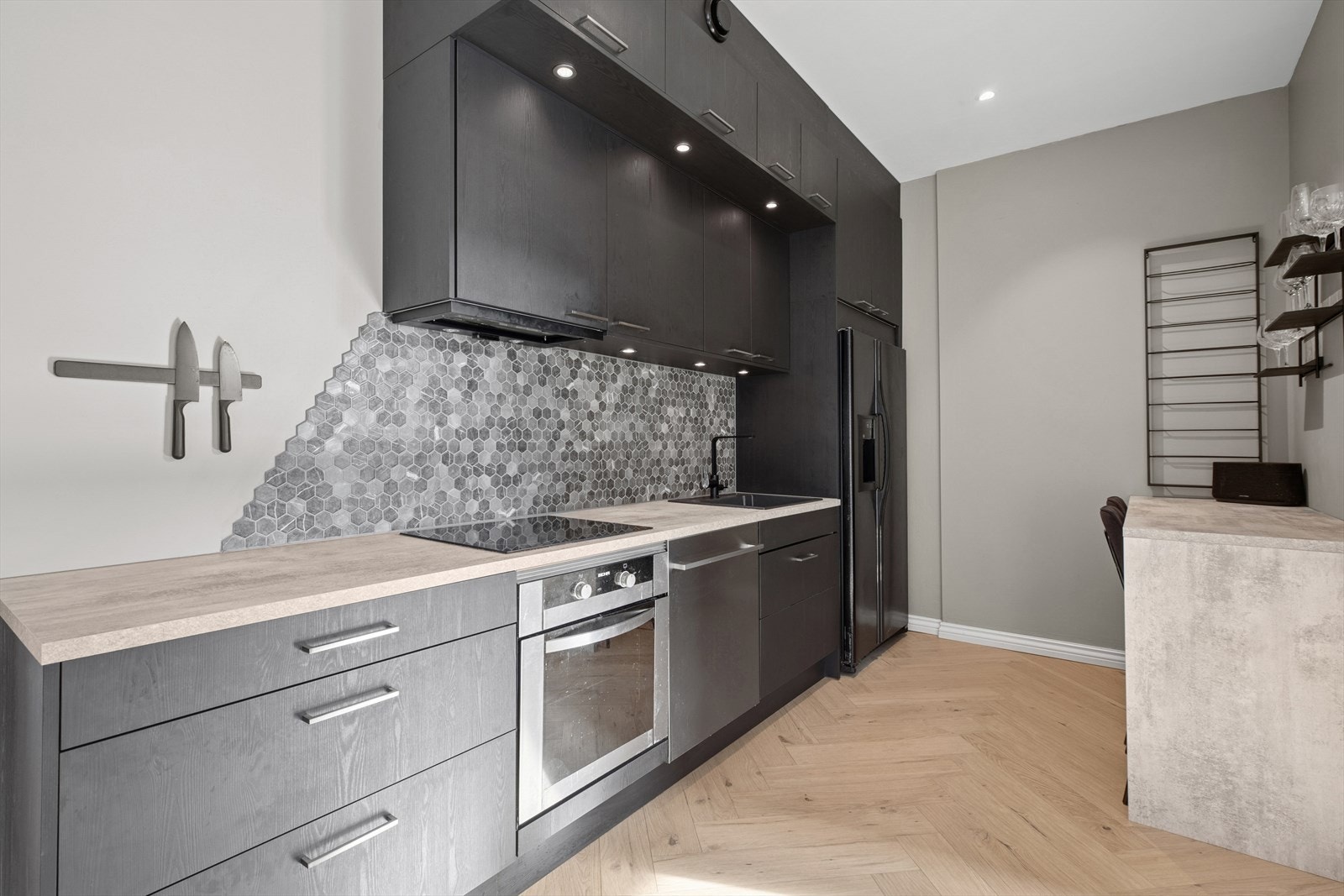 Det er innfelte LED-lys under overskap og fliser på vegg over kjøkkenbenk. Galleribilde