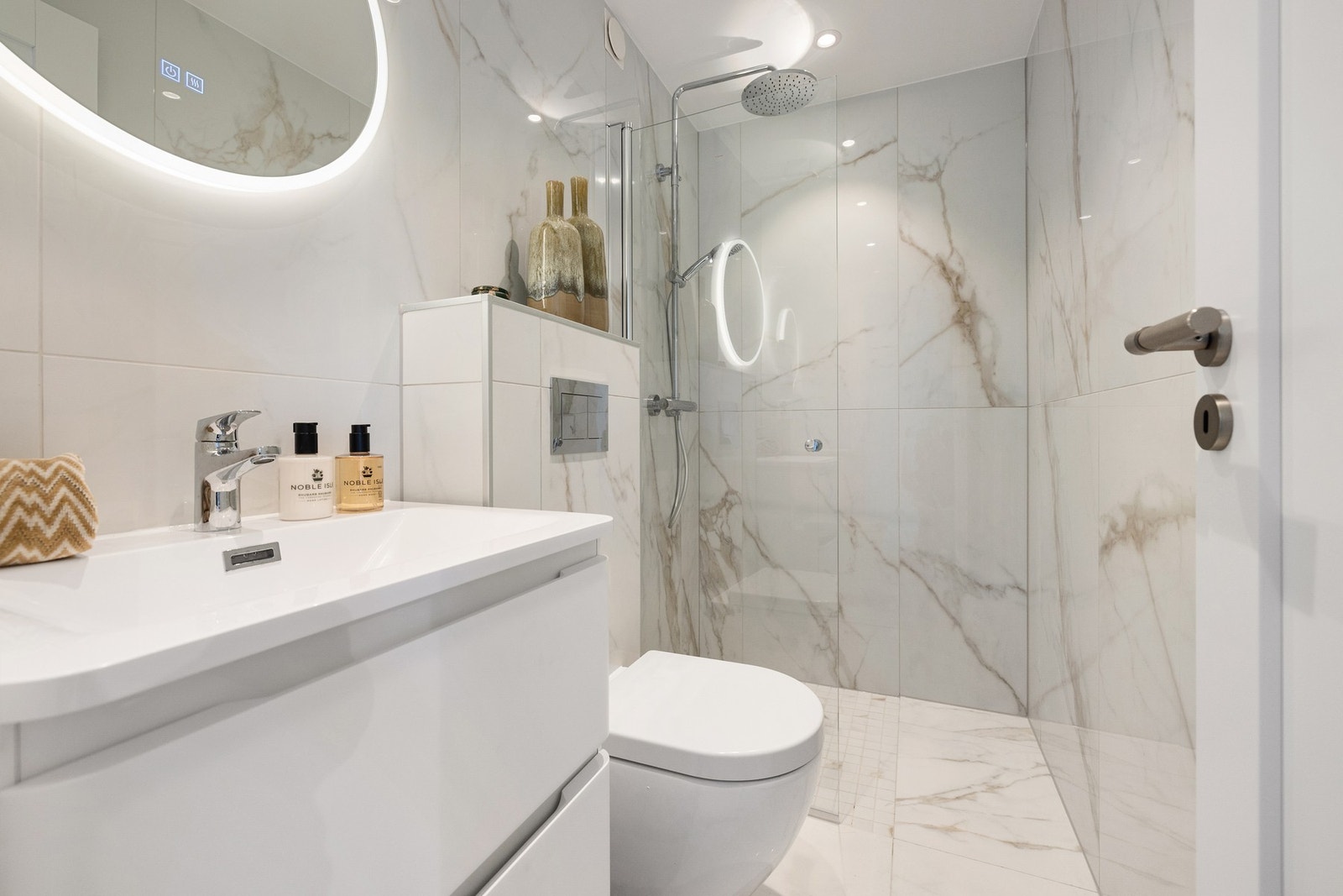 Badet er utstyrt med en moderne servant hvor det er godt med oppbevaringsmuligheter for toalettsaker, toalett og en dusjsone som er avskjermet med en elegant dusjvegg. Galleribilde